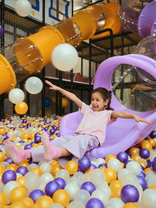 A young girl happily playing in play area by coming down the slide